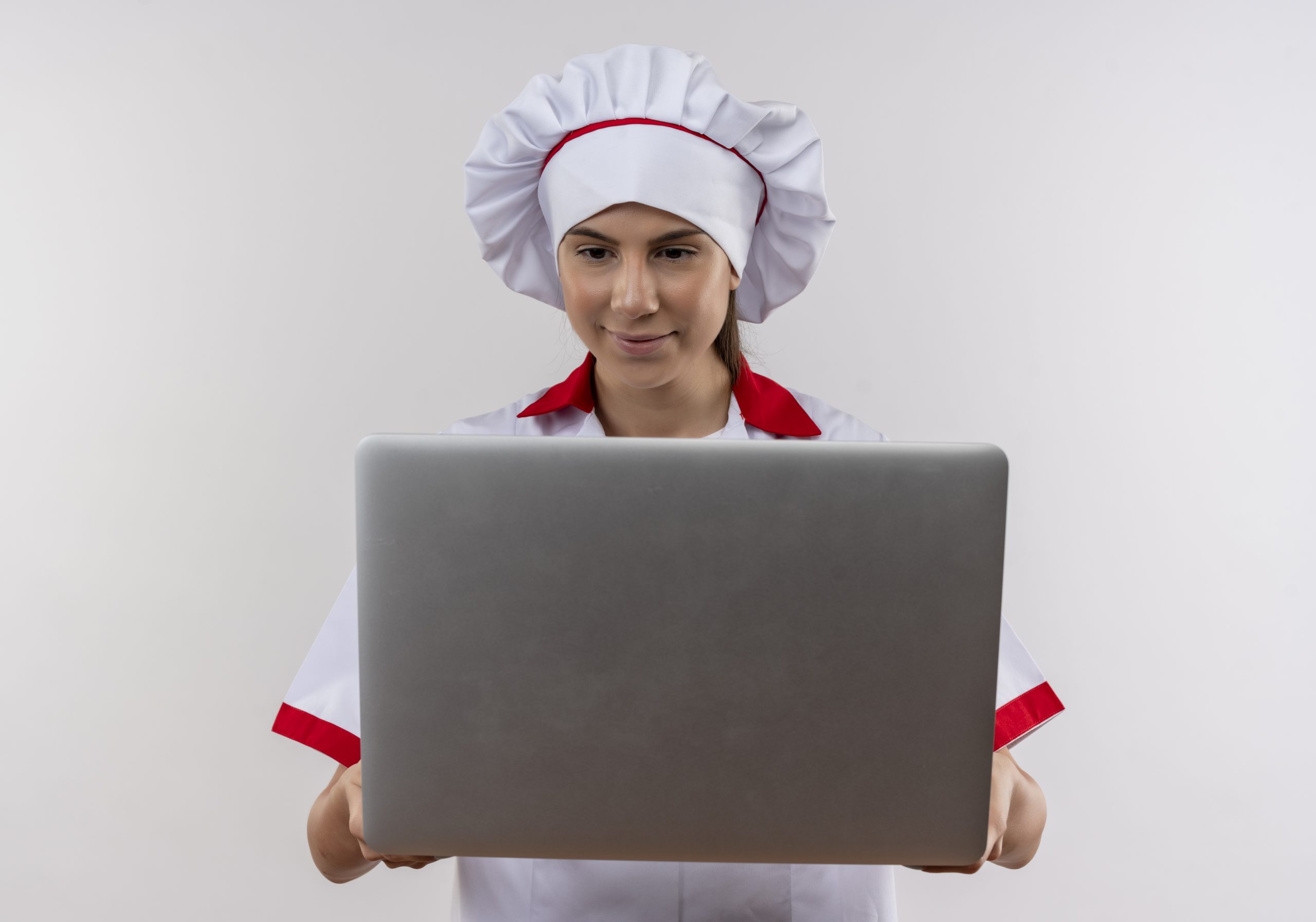 young pleased caucasian cook girl in chef uniform holds and looks at laptop isolated on white background with copy space